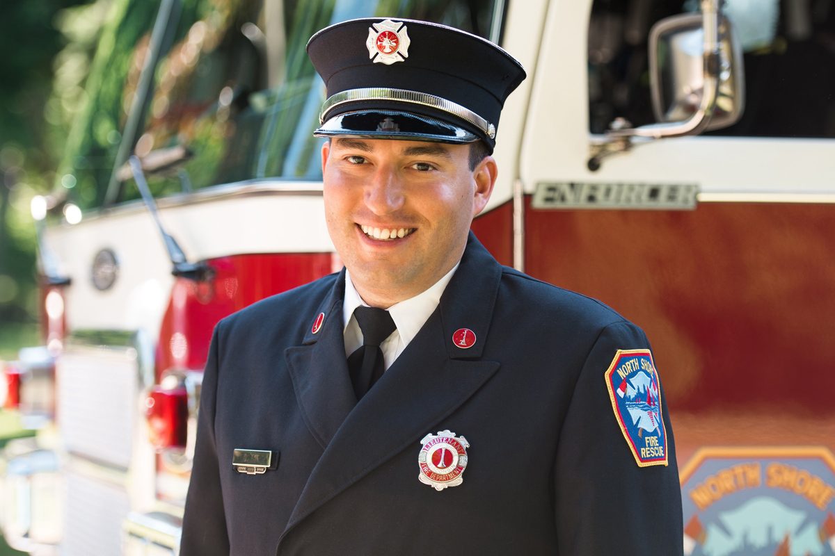 Daniel Tyk smiles at the camera wearing his Lieutenant uniform in front of a fire truck