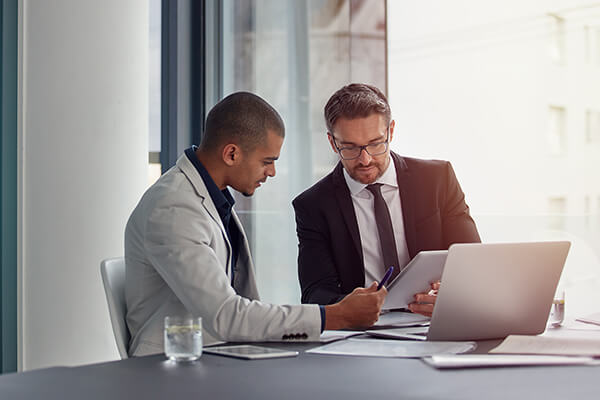 Two men look at a tablet together during a business meeting.