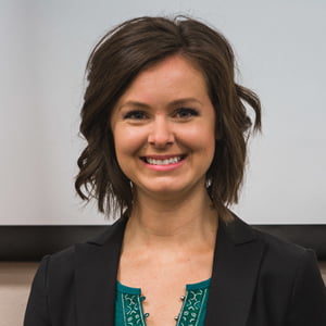 A young Caucasian woman with medium brown hair smiles. She is wearing a green top with a black blazer.