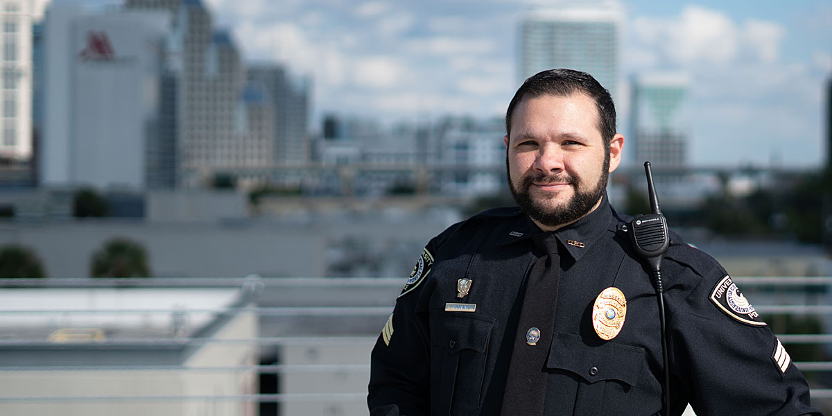 police officer smiling and posing in front of a faded city skyline in the background