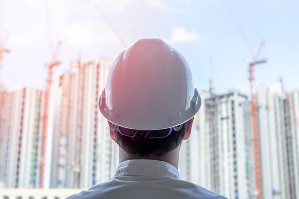 A man in a hardhat has his back turned to look at a construction site.