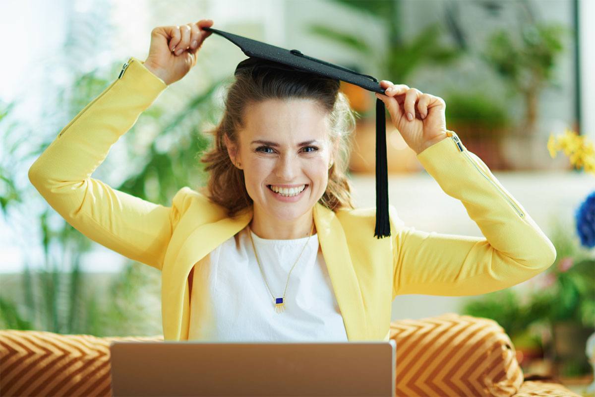 A woman cheerfully reaches up to grab her graduation cap.