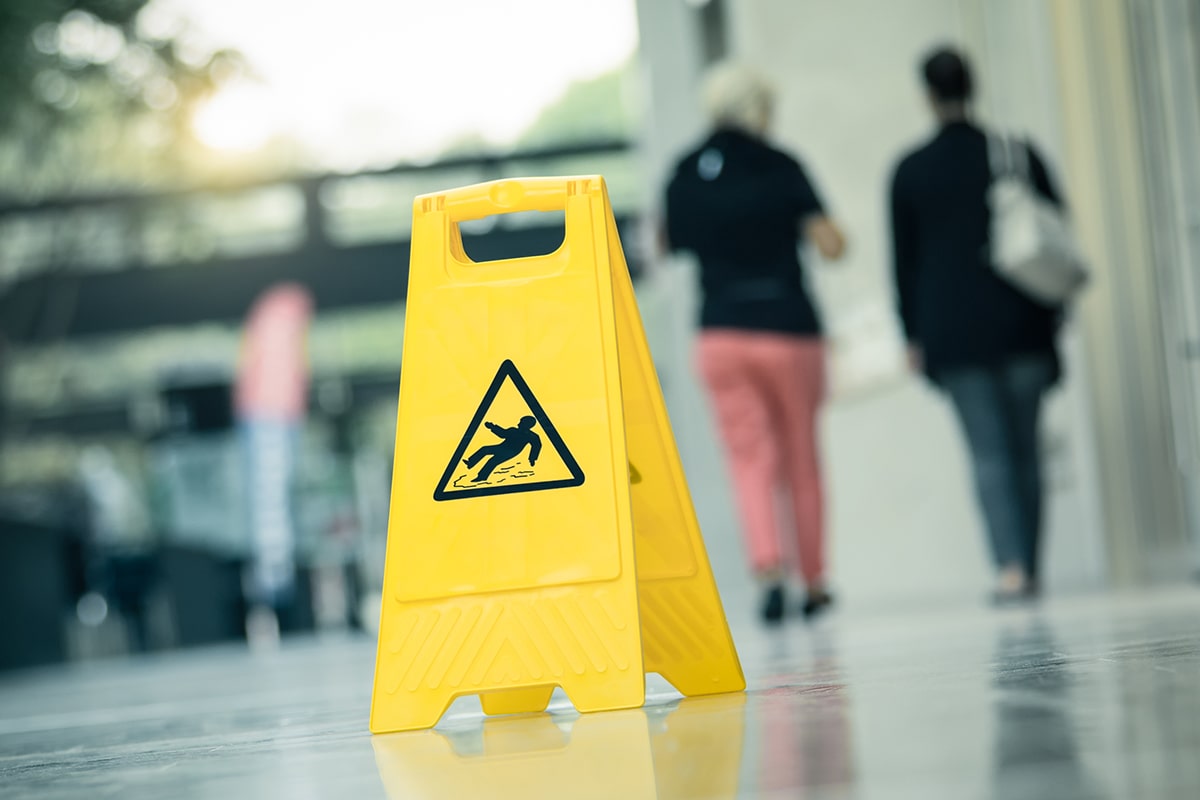 A yellow warning sign "slippery" with walking people in the background