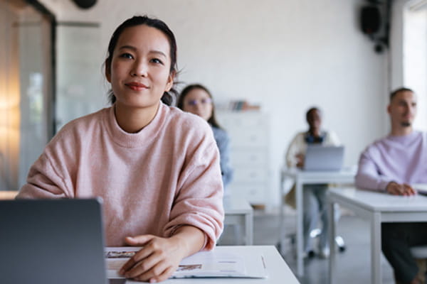 Woman in light pink sweater sitting at desk in class room