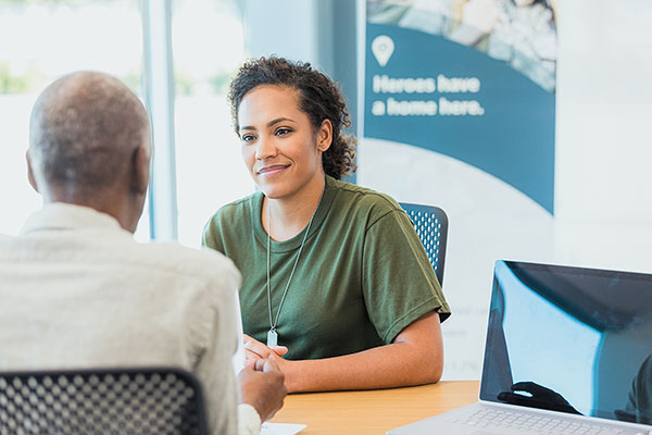 Military veteran sitting at a desk across from a mentor and discussing online universities