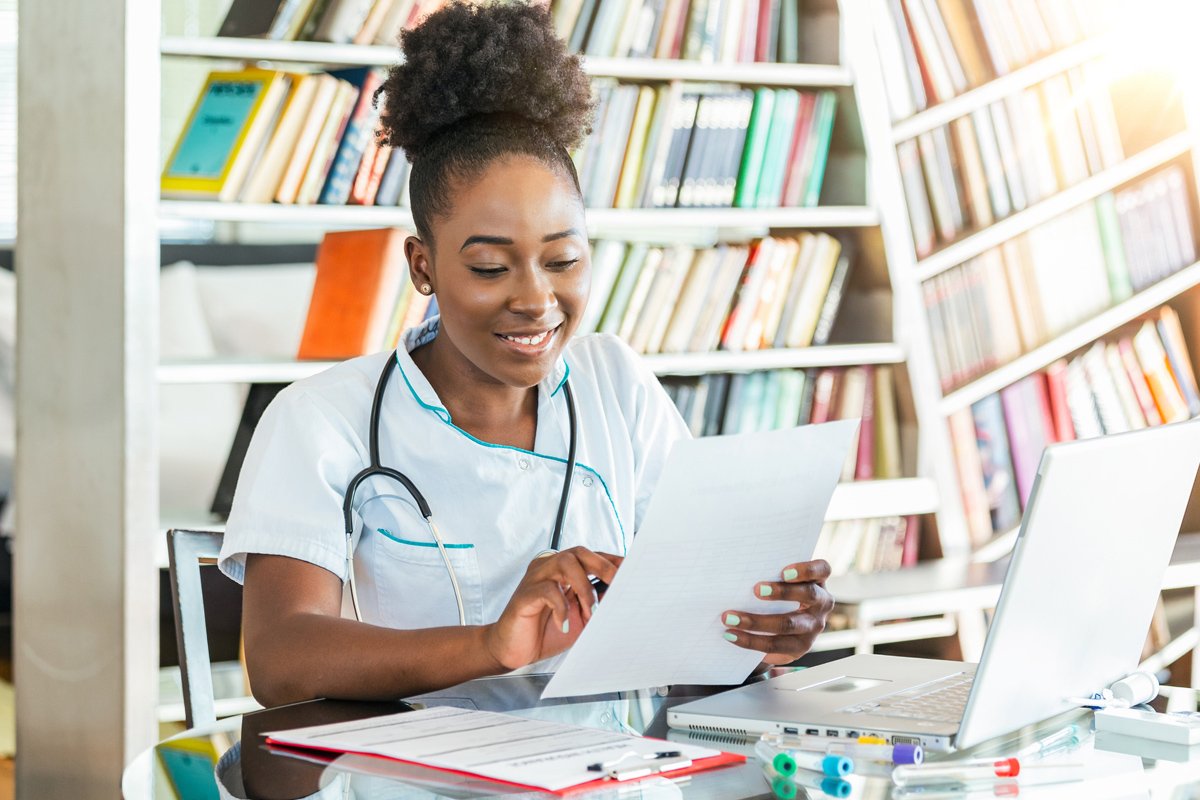 A young woman in scrubs looks over paperwork.