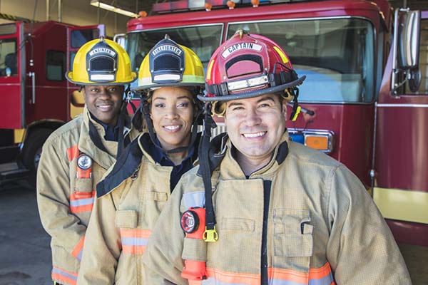 three firefighters posing in front of a fire truck parked inside the fire station