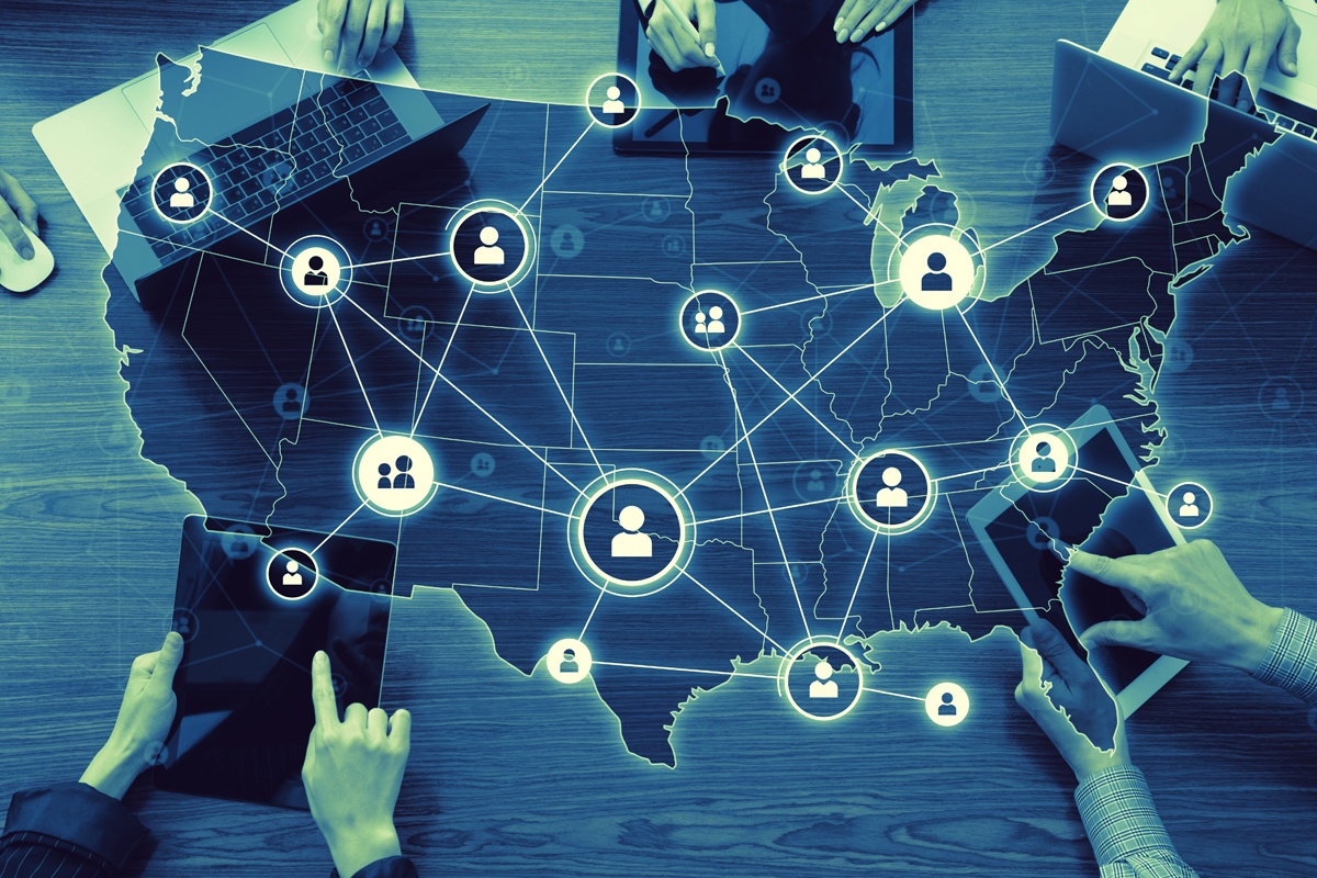 US map with network of user icons overlays a table with several people using laptops and tablets.