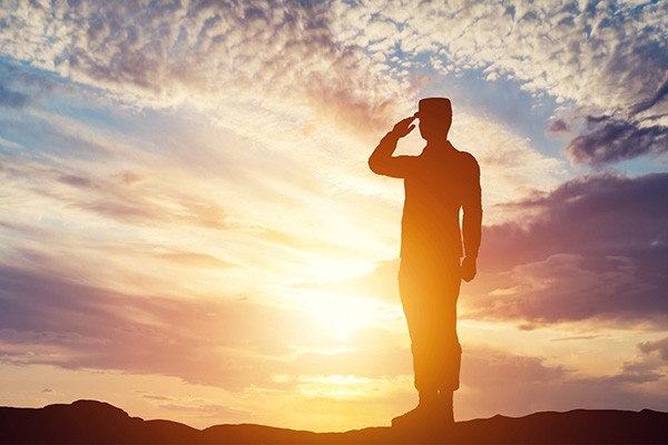 Silhouette of a soldier saluting against a sunset.