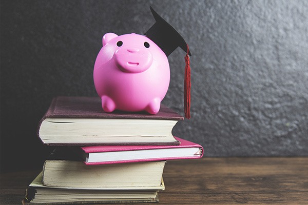 Graduation cap sits on a piggy bank standing on a stack of books.