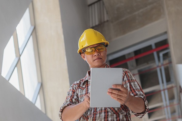 A man in safety glasses and hard hat holds a tablet.