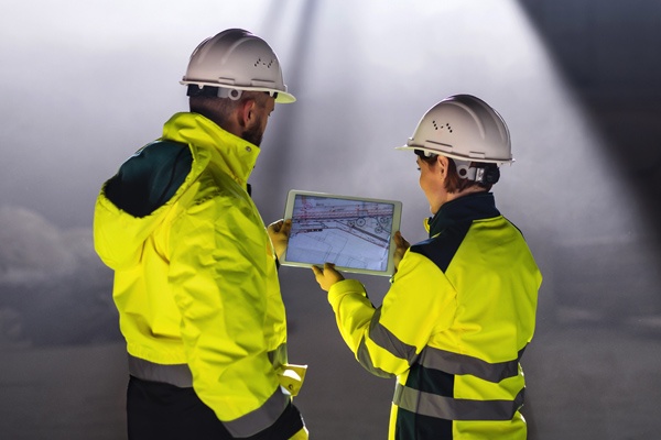 Two safety workers look at plans on a tablet.