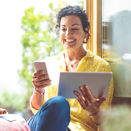 Student smiles happily while holding both phone and tablet.