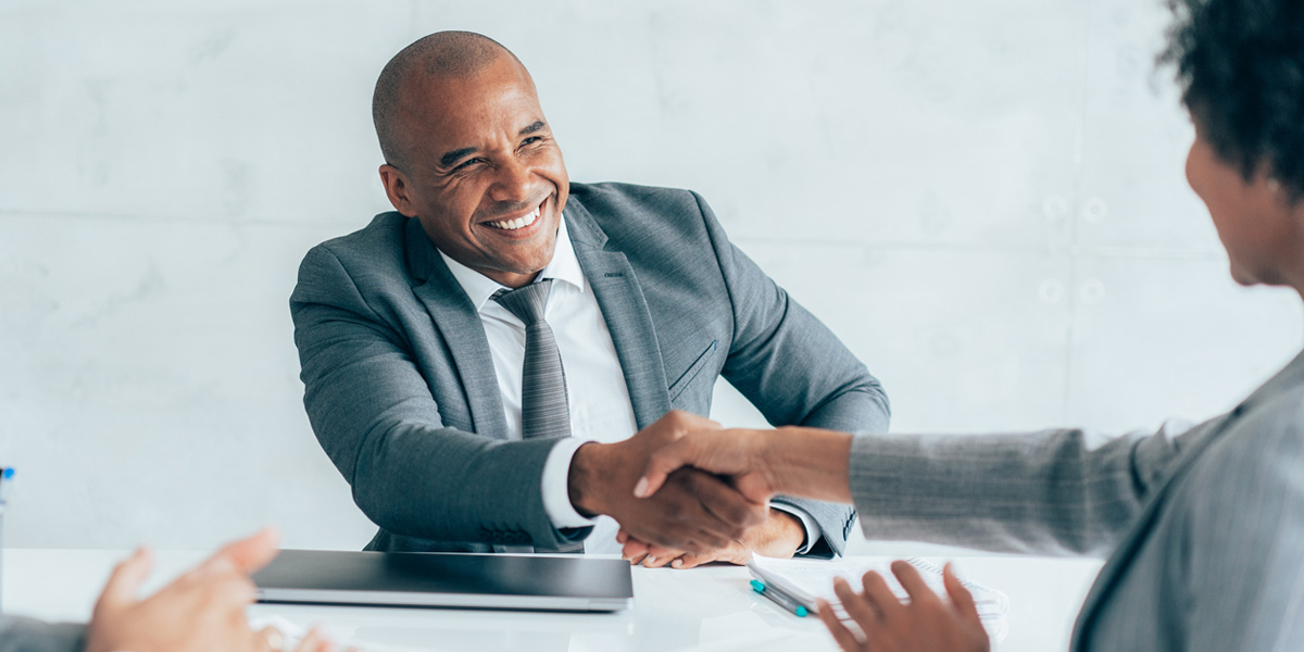 military veteran smiling and sitting across the table from a person while shaking hands with them