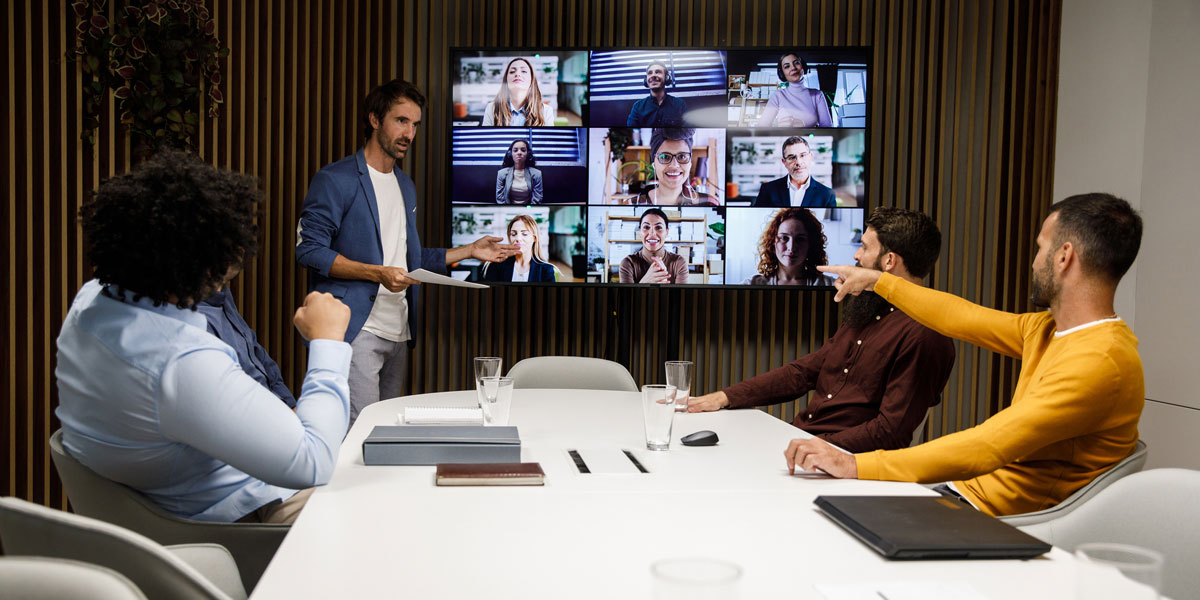 business professionals in a conference room interacting with colleagues in a video chat displayed on a large wall-mounted screen