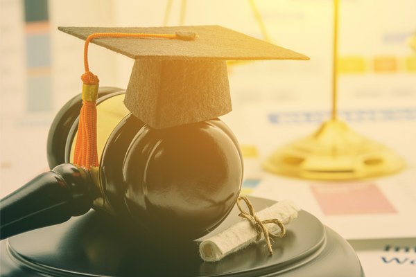 A miniature graduation cap sits atop a gavel resting next to a miniature diploma.