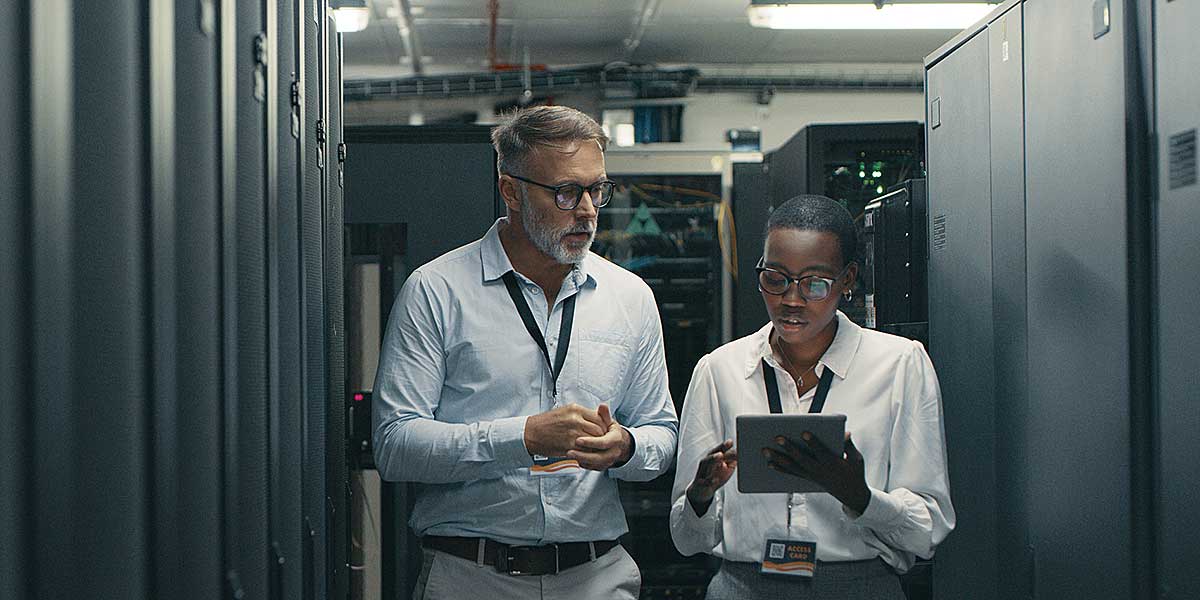 two homeland security professionals standing in a data center and reviewing information on a tablet