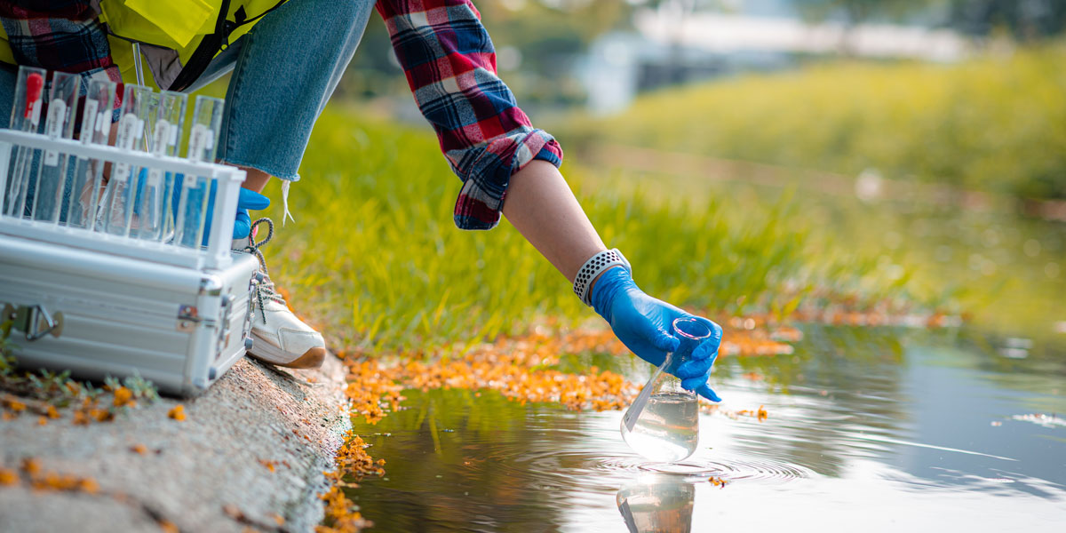 close image of environmental management professional's arm collecting a water sample at an outdoor site