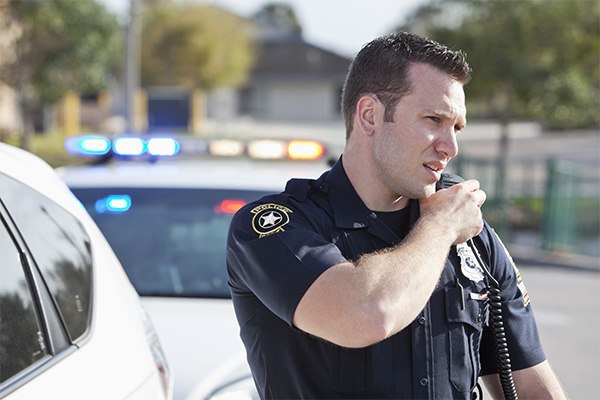 A police officer talks into a walkie talker on his shoulder.