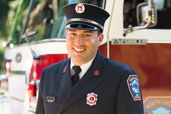 Daniel Tyk smiles at the camera wearing his Lieutenant uniform in front of a fire truck