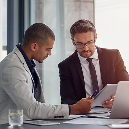 Two professionals in business suits discuss notes.