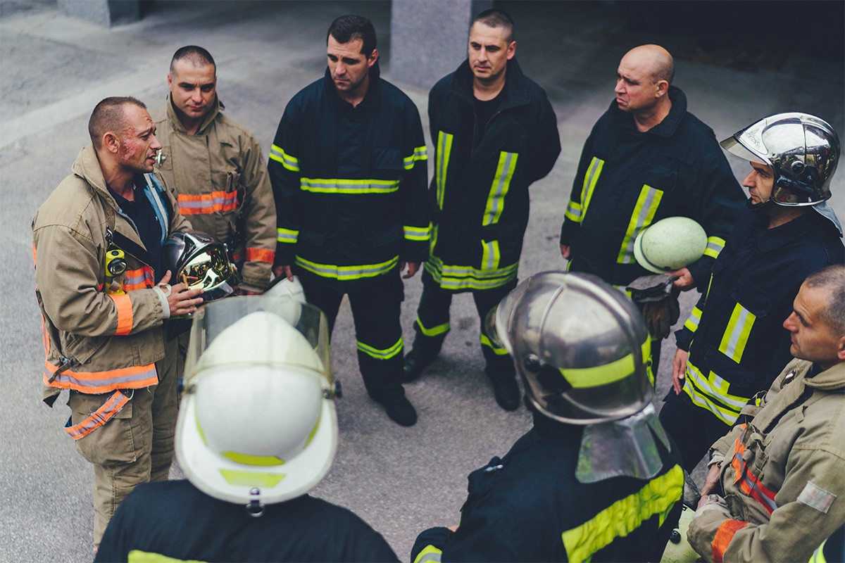 A group of firefighters stand in a circle as one speaks to them all.