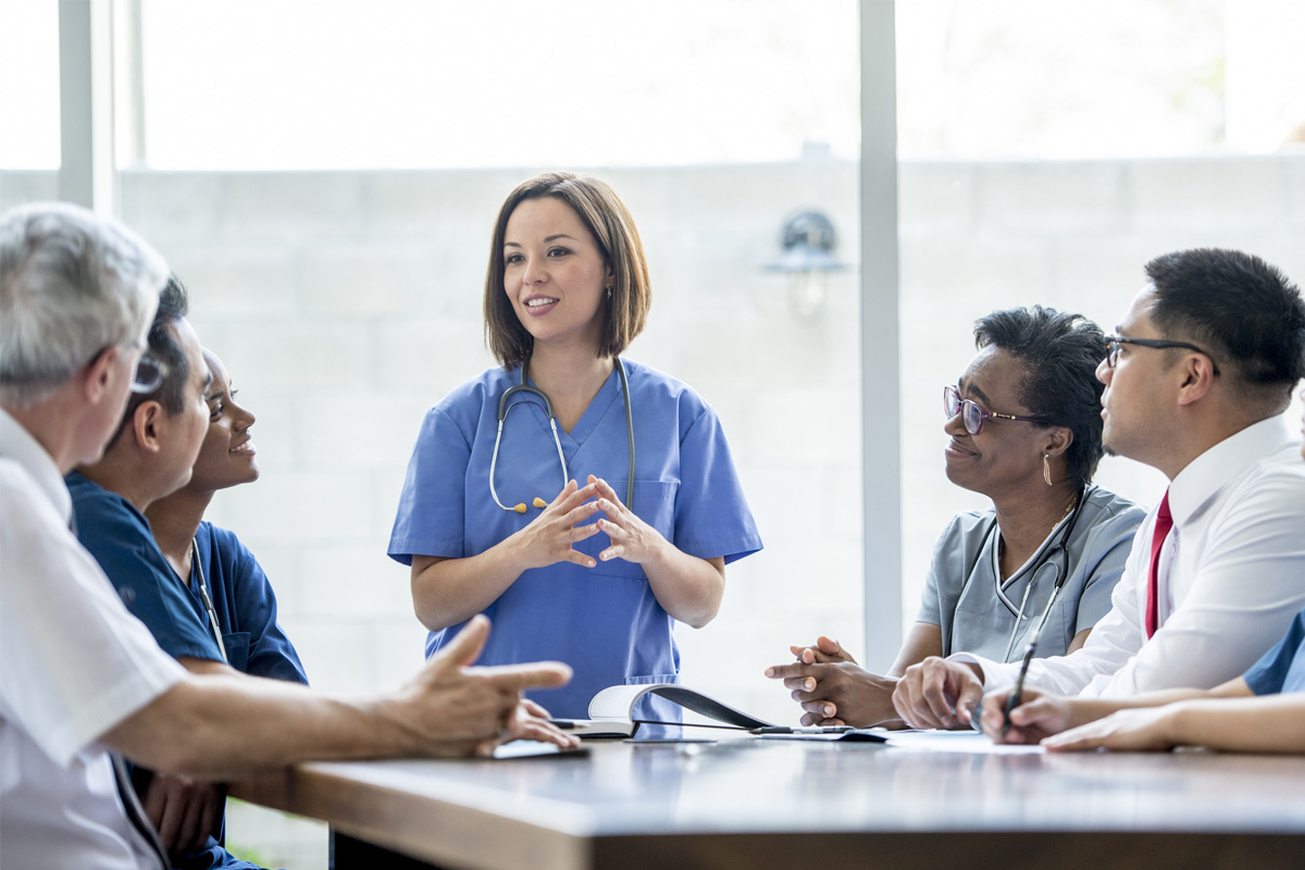 public health professional wearing scrubs while standing and talking to a group of colleagues