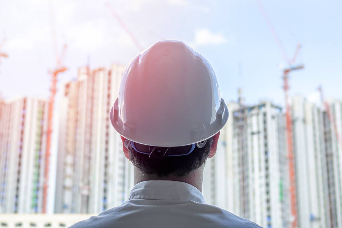 A man in a hardhat has his back turned to look at a construction site.
