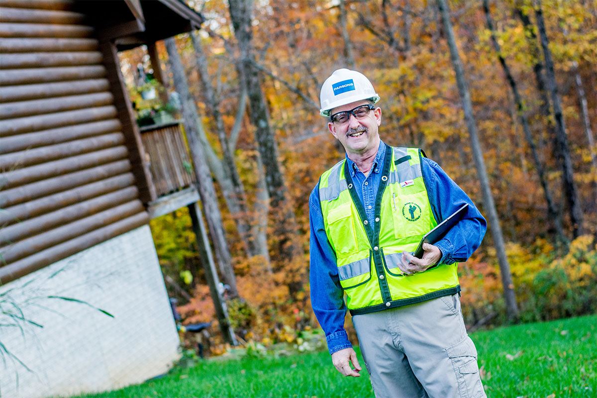 Dan Hughes smiles in a safety vest and hard hat as he holds a tablet.