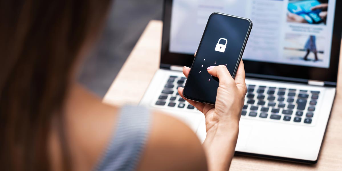 point of view of person entering a password on a mobile phone and sitting at a desk in front of a laptop