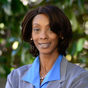 African American woman with shoulder length hair, professionally dressed in grey suit smiles at camera.