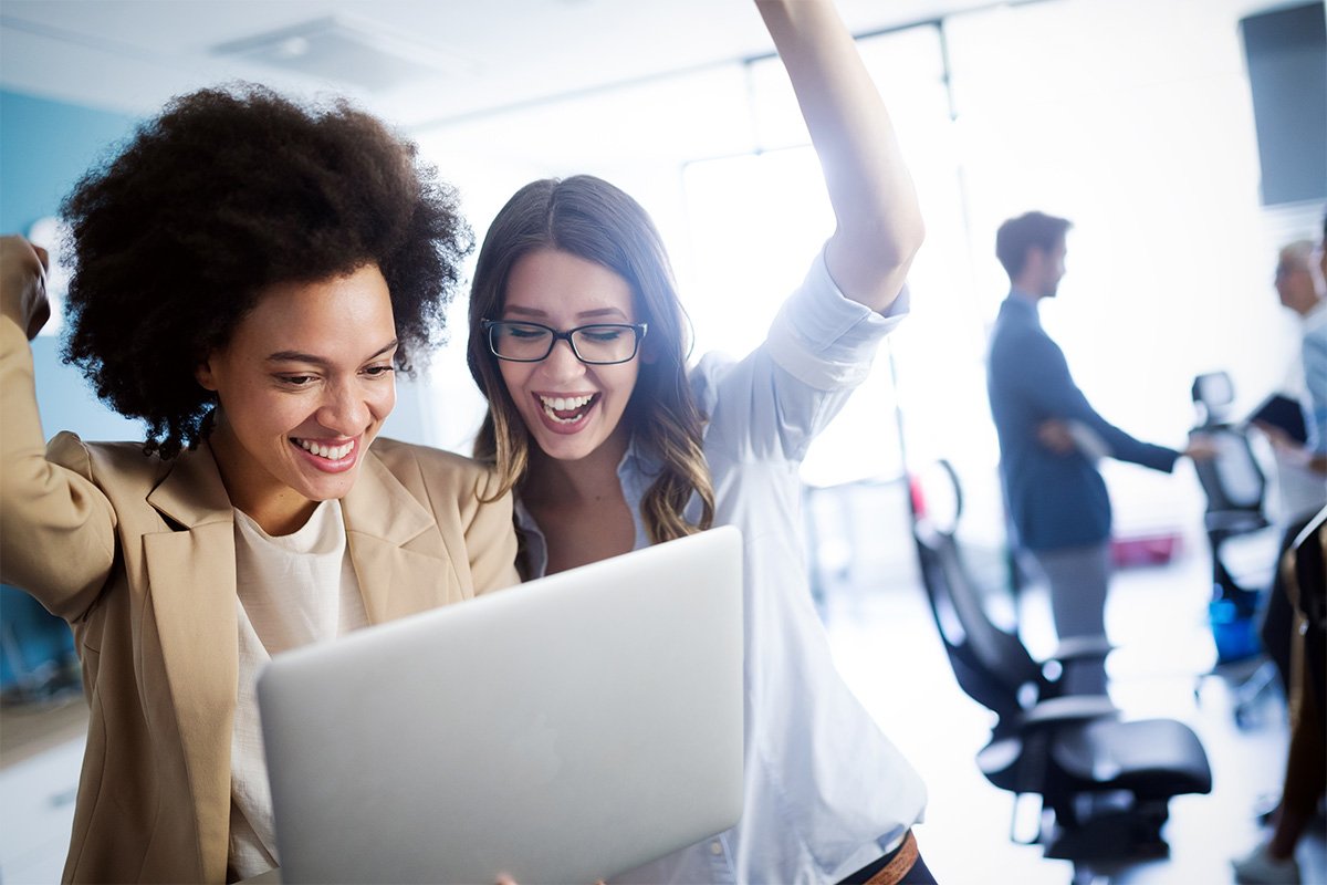 Two women cheer as they look at a laptop together.