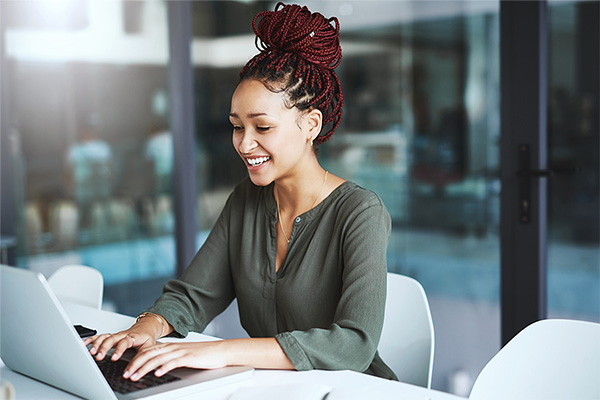 Smiling student sitting at a desk and using a laptop computer for a self-paced online college degree program