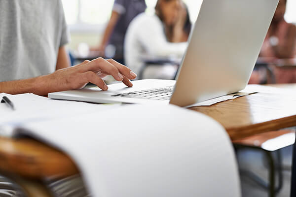 Close up of open notepad next to someone using a laptop.