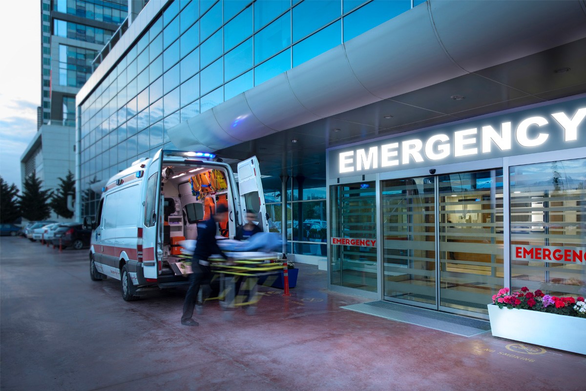A blurred scene of two EMTs unloading a gurney from an ambulance at an emergency room entrance.