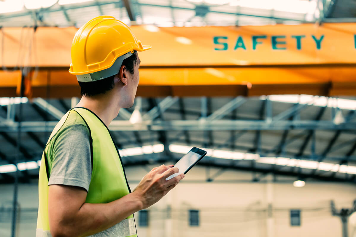 A safety professional wearing a yellow hard hat and holding a tablet