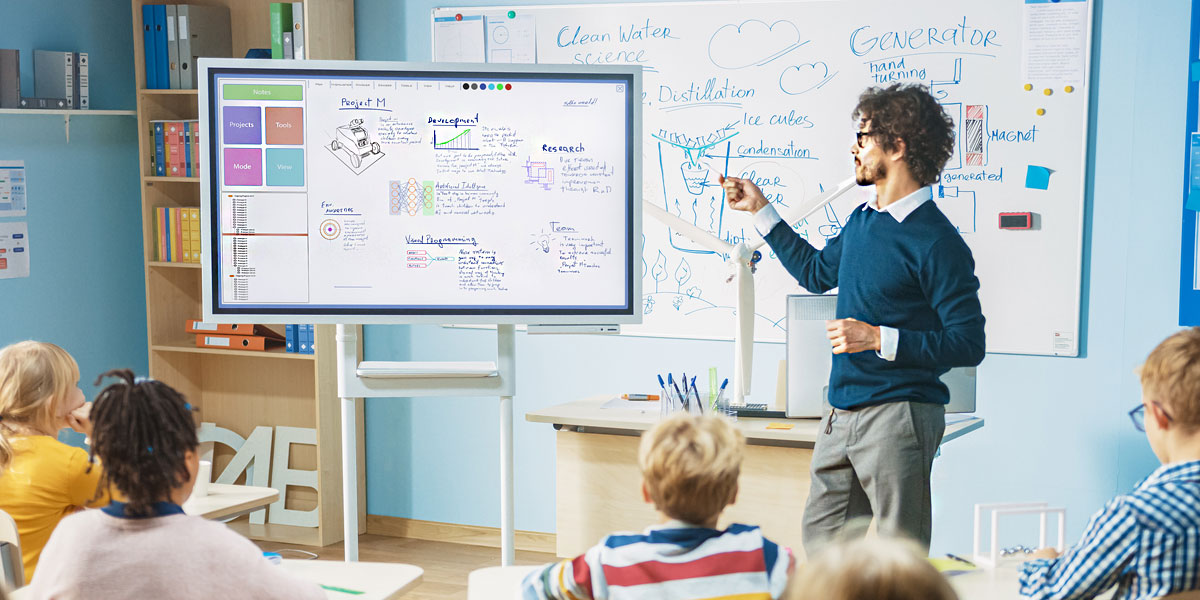 instructor standing in front of a digital screen in a classroom and presenting information to students