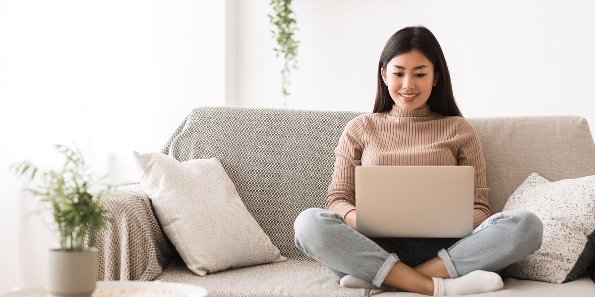 college student sitting on couch and holding laptop